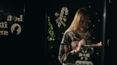 Noel zamanı, sıcak tatil ışıklarıyla aydınlatılmış cam bir pencereye şenlikli tasarımlar çizen genç bir kadın. Yüksek kalite 4k görüntü