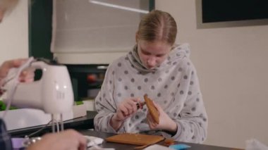 Kapüşonlu kapüşonlu kapüşonlu genç bir kız modern bir mutfakta zencefilli kurabiyelerle odak ve hassasiyetle süslüyor. Yüksek kalite 4k görüntü