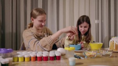 Güzel dekore edilmiş paskalya pastası, beyaz kremalı, renkli serpiştirmeler, ve kırmızı yumurtalarla çevrili yanan bir mum, bir insan masadaki eşyaları ayarlarken. Yüksek kalite 4k görüntü