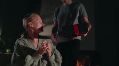 Sıcak bir şöminenin yanında oğlundan sürpriz bir hediye alan orta yaşlı bir kadın duygulanmış görünüyor. Yüksek kalite 4k görüntü