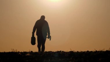 Gün batımında ya da gün doğumunda parlak güneşe karşı aletler tutan bir çiftçinin silueti. Sahne, doğa ve tarım çalışmalarıyla barışçıl bağlantıyı vurgulayarak, yalnızlığı ve kırsal yaşamı aktarıyor.