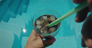 Güneşli bir günde, elinde bir bardak buzlu kolayla yüzme havuzunda dinlenen bir insanın görüntüsü. Yüksek kalite 4k görüntü