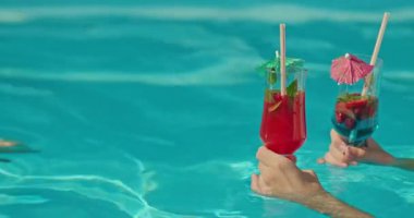Yüzme havuzunda tropikal kokteyller içen iki el berrak mavi suya karşı ferahlatıcı bir yaz anının tadını çıkarıyor. Yüksek kalite 4k görüntü