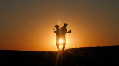 Orta yaşlı bir kadının siluetleri ve yetişkin oğlu gün batımında kırsal bir alanda neşe içinde dans ediyorlar, neşeli ve enerjik bir anı paylaşıyorlar. Yüksek kalite 4k görüntü