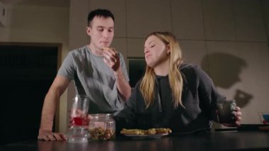 Genç bir çift, avokado tostunu modern bir mutfakta, guacamole ile birlikte yiyor ve sıradan bir yemek yiyorlar. Yüksek kalite 4k görüntü