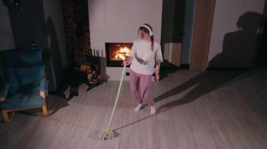 Genç bir kadın temizliği dansa çeviriyor. Kulaklıkla müzik dinlerken paspasla enerji dolu bir şekilde hareket ediyor. Beyaz tişört, pembe eşofman altı ve beyaz çoraplar giyiyor.