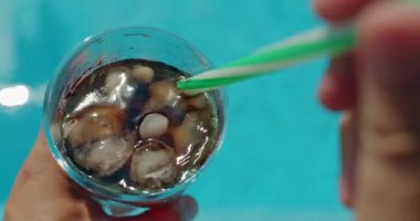 Güneşli bir günde soğuk bir bardak buzlu kolayı yudumlayan kişi, içecek olarak pipetini tutuyor. Yüksek kalite 4k görüntü