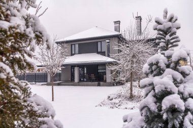 Karla kaplı çatısı ve verandası karla kaplı ağaçlar ve kozalaklı ağaçlarla çevrili modern iki katlı bir ev. Yüksek kalite fotoğraf