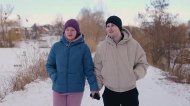 Genç çift karlı bir yolda el ele yürüyor, gülümsüyor ve aydınlık bir kış gününde birbirlerine eşlik ediyorlar. Yüksek kalite 4k görüntü