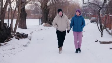 Genç çift karlı bir yolda el ele yürüyor, gülümsüyor ve çıplak ağaçların ve sakin bir manzaranın ortasında kış yürüyüşünün tadını çıkarıyor. Yüksek kalite 4k görüntü