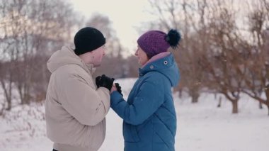 Karlı bir yolda yürürken el ele tutuşan ve gülümseyen genç çift neşeli bir kış gününün tadını çıkarıyor. Yüksek kalite 4k görüntü