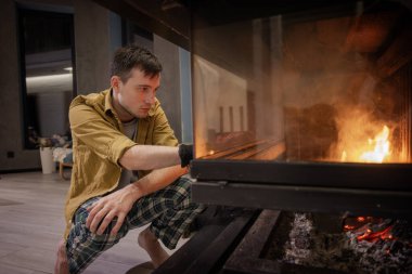 İçeride şömineyi aydınlatan genç bir adam, odaklanmış ve özenli, günlük ev kıyafetleri giymiş. Yüksek kalite fotoğraf