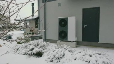 Karla kaplı bitkilerle çevrili modern bir evin dışındaki ısı pompası kış enerjisinin verimliliğini gösteriyor. Yüksek kalite 4k görüntü