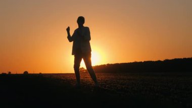 Gün batımında kırsal bir alanda neşeyle dans eden orta yaşlı bir kadının silueti tasasız ve tasasız bir anı kucaklıyor. Yüksek kalite 4k görüntü
