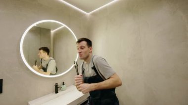 Oyuncu teknisyen modern bir banyoda ingiliz anahtarıyla dans ederek mizahi ve enerjik bir sahne yaratıyor. Yüksek kalite 4k görüntü
