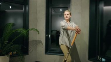 Genç bir kadın, modern minimalist bir iç mekanda evinde paspasla şakça dans ediyor. Yüksek kalite 4k görüntü