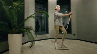 Genç bir kadın, modern minimalist bir iç mekanda evinde paspasla şakça dans ediyor. Yüksek kalite 4k görüntü