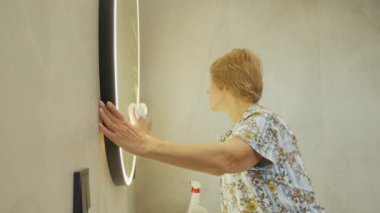 Üst düzey bir kadın, leke bırakmayan bir yansımayı garantilemek için banyo aynasını bezle temizliyor. Yüksek kalite 4k görüntü