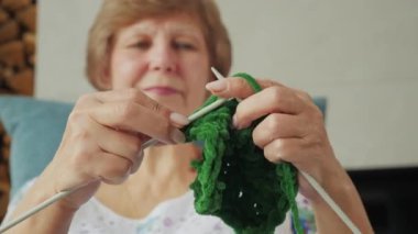 Yaşlı kadınların elleri pelüş yeşil iplikle örgü örerken, dikişlerin hassas dokusunu ve konsantre yüz ifadesini vurguluyor. Yüksek kalite 4k görüntü