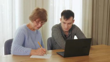 Üst düzey kadın notlar yazarken, genç adam dizüstü bilgisayarda bir şeyler anlatıyor. İyi aydınlatılmış bir odada, ahşap bir masada birlikte oturuyorlar. Yüksek kalite 4k görüntü