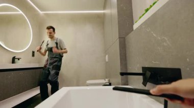 Modern bir banyoda dans eden oyuncu bir muslukçu bir el küveti duş başlığıyla doldururken, esprili bir şekilde özel dans ediyor. Yüksek kalite 4k görüntü