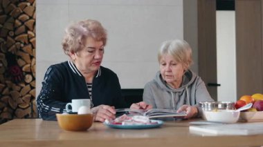 İki son sınıf öğrencisi, ahşap bir masada oturup yemek tarifi kitabını tartışırken sıcak ve rahat bir evde yemek pişirmek için gerekli malzemeleri hazırlıyorlar. Yüksek kalite 4k görüntü