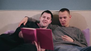 İki genç adam bir yatağa yakın oturuyor, samimi ve samimi bir atmosferde kitap okuyorlar. Yüksek kalite 4k görüntü