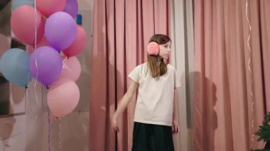 Pembe perdelerin yanında elinde balonlarla dolaşan, pembe kulaklık takan ve sıradan kıyafetler giyen genç bir kız. Yüksek kalite 4k görüntü