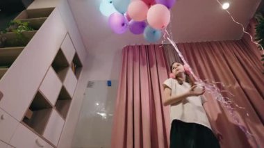 Pembe perdeler ve balonların yanında dönen pembe kulaklıklar takan ve sıradan kıyafetler giyen genç bir kız. Yüksek kalite 4k görüntü