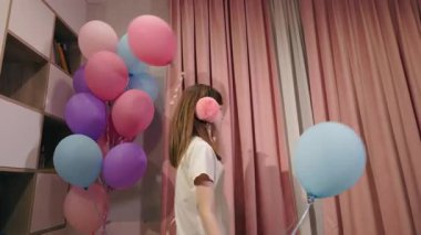 Genç kız neşeli bir şekilde balonları pembe perdeleri ve kulaklıkları olan kapalı bir alanda tutuyor. Yüksek kalite 4k görüntü