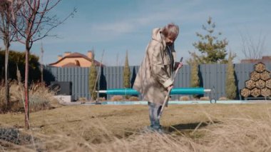 Yaşlı bir kadın bahçedeki çimenleri ve yaprakları tırmıklayıp bahar için çimenleri hazırlıyor. Yüksek kalite 4k görüntü