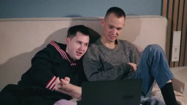 Yatakta uzanmış laptopa dikkatle bakan iki genç adam samimi ve samimi bir anı paylaşıyorlar. Yüksek kalite 4k görüntü