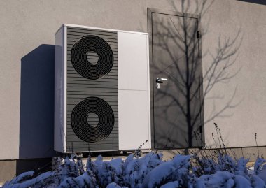 Kışın, etrafı karla kaplı bitkilerle çevrili bir konut binasının dışına kurulmuş modern ısı pompası. Soğuk havada enerji tasarruflu ısıtma çözeltisi. Yüksek kalite fotoğraf