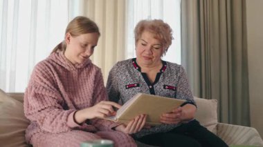 Büyükannem ve torunum bir kanepede oturup aile albümümüze bakıp geçmişi yâd ederken gülümsüyorlar. Yüksek kalite 4k görüntü
