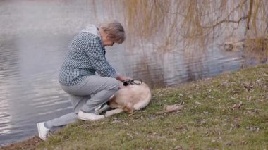 Yaşlı bir kadın gölün kenarındaki çimlerin üzerinde diz çöküp Golden Retriever 'ını okşuyor. Köpek sırtüstü döner, anın tadını çıkarır. Söğüt dalları durgun suların üzerinde asılı