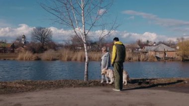 Yaşlı bir kadın ve torunu kırsal bir göl kenarında Golden Retriever 'larıyla yürüyüşe çıkıyorlar. Genç adam yakınlarda dururken kadın köpeği okşar. Bir kilise ve köy evleri görülebilir.