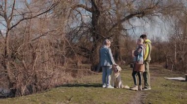 Yaşlı bir kadın, yetişkin kızı ve torunu güneşli bir bahar gününde Golden Retriever 'larıyla yürüyüşe çıkıyorlar. Sohbet etmek için dururlar, kırsal alanın tadını çıkarırlar. Yüksek kalite 4k