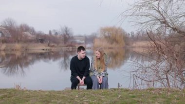 Genç bir adam ve bir kadın, sessiz bir iskelede oturur, sakin göl kıyısında yansımalarını seyrederler. Yüksek kalite 4k görüntü