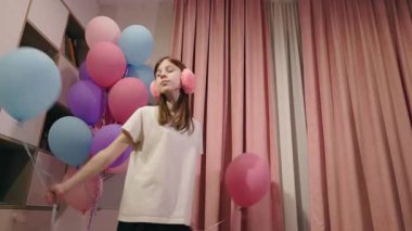 Genç kız, pembe perdeleri ve kulaklıkları olan rahat bir yerde balon tutuyor. Yüksek kalite 4k görüntü