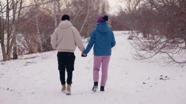 Genç çift, karlı bir arazide, bir ağacın kenarında hassas bir anı paylaşıyor, hafif kar yağışının tadını çıkarıyor ve birbirlerine şefkat ve sevgiyle eşlik ediyorlar.