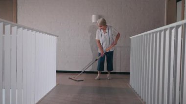 Modern bir ev içinde ahşap zemini paspaslayan yaşlı bir kadın, temizlik ve bakım üzerine odaklanmış. Yüksek kalite 4k görüntü