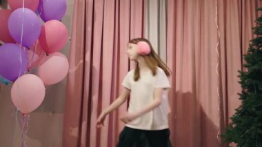 Pembe kulaklık takan genç kız pembe perdeler ve balonların yanında dans ediyor. Yüksek kalite 4k görüntü