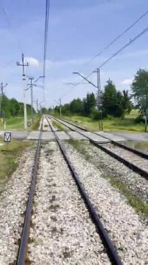 Açık mavi gökyüzüyle güneşli bir yaz gününde yeşil çimenler ve ağaçlarla çevrili düz demiryolu rayları. Yüksek kalite 4k görüntü