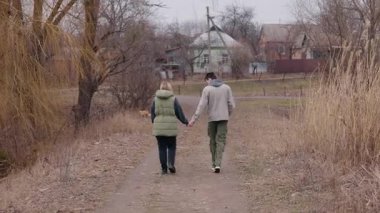 Genç bir çift bulutlu bir bahar gününde kirli bir patika boyunca el ele yürür. Kırsal alanda yürürken kalın giysiler giyerler. Yüksek kalite 4k görüntü