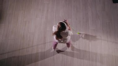 Yukarıdan bakıldığında genç bir kadın temizlik yaparken paspasla enerjik bir şekilde dans ediyor. Beyaz kapüşonlu, pembe eşofmanlı, beyaz çoraplı, hareketli kulaklıklarla müzik dinliyor.