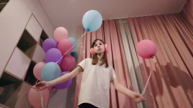 Pembe perdeleri ve kulaklıkları olan neşeli bir iç mekanda balon tutan genç kız. Yüksek kalite 4k görüntü
