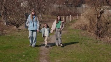 İki genç kız, açık bir bahar gününde aralarında küçük bir çocukla birlikte bir köy yolunda yürürler, el ele tutuşurlar ve gün ışığında gülümserler. Yüksek kalite 4k görüntü