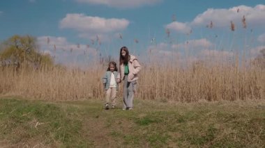 İki küçük kız, uzun kuru kamışlarla ve açık mavi gökyüzüyle çevrili ılık bir bahar gününde birlikte doğayı keşfederken el ele tutuşuyorlar. Yüksek kalite 4k görüntü