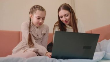 Genç bir kadın ve küçük kız kardeşi dizüstü bilgisayarlarını kullanarak yatakta oturuyor ve evde vakit geçiriyorlar. Yüksek kalite 4k görüntü