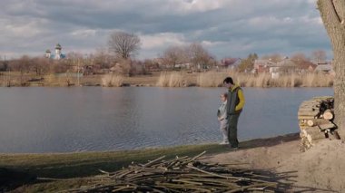 Yaşlı bir kadın ve torunu, sazlıklarla çevrili kırsal bir nehir kıyısında ve bulutlu bir gökyüzünün altında kilise olan uzak bir köyde yürüyorlar. Yüksek kalite 4k görüntü